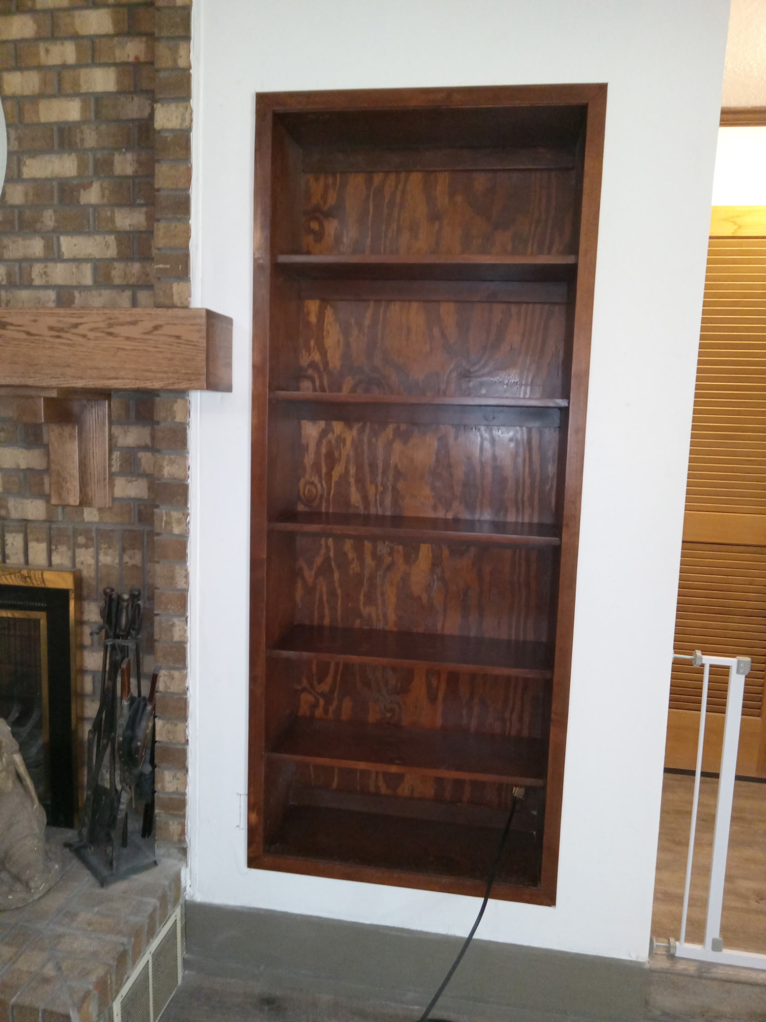 Stained recessed bookcase built into a wall next to a brick fireplace.
