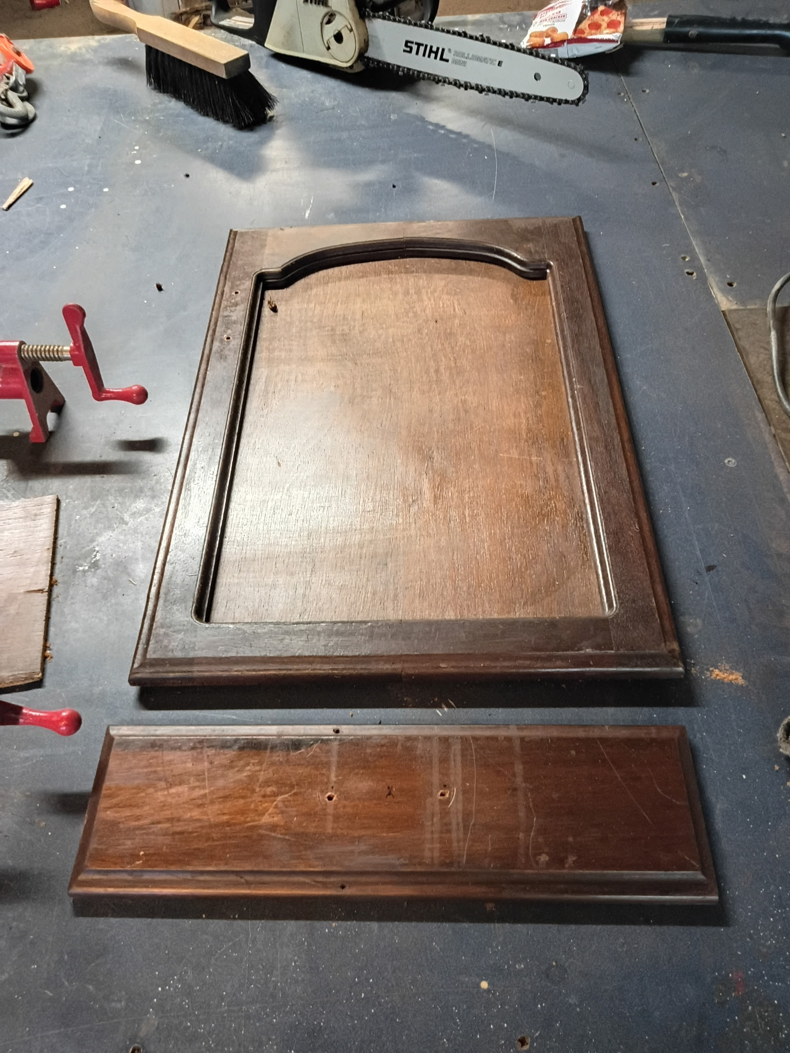 Refinished arched cabinet door panel on a workbench beside a chainsaw.