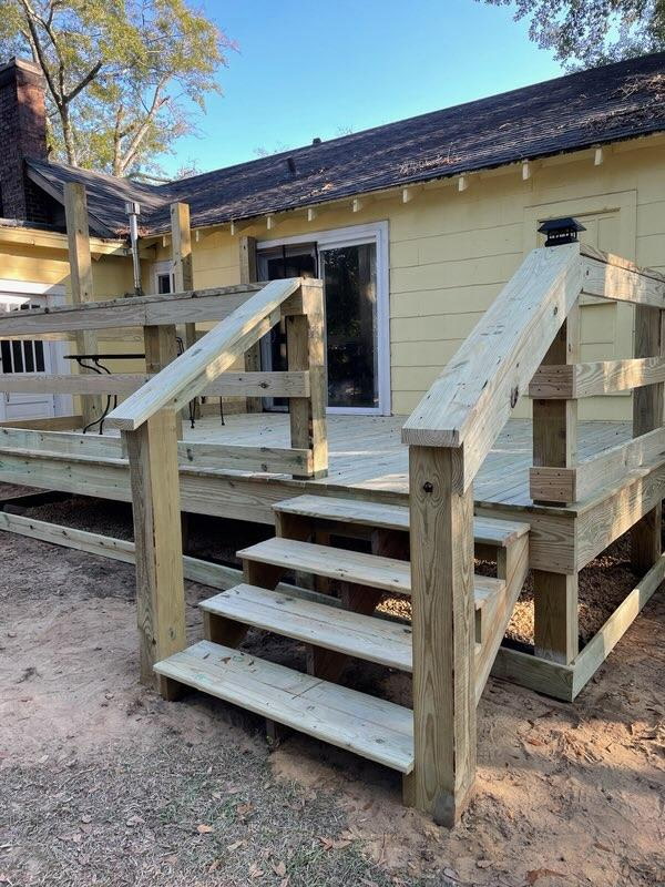 Newly framed pressure-treated deck with stairs and railings on a yellow Craftsman-style house.