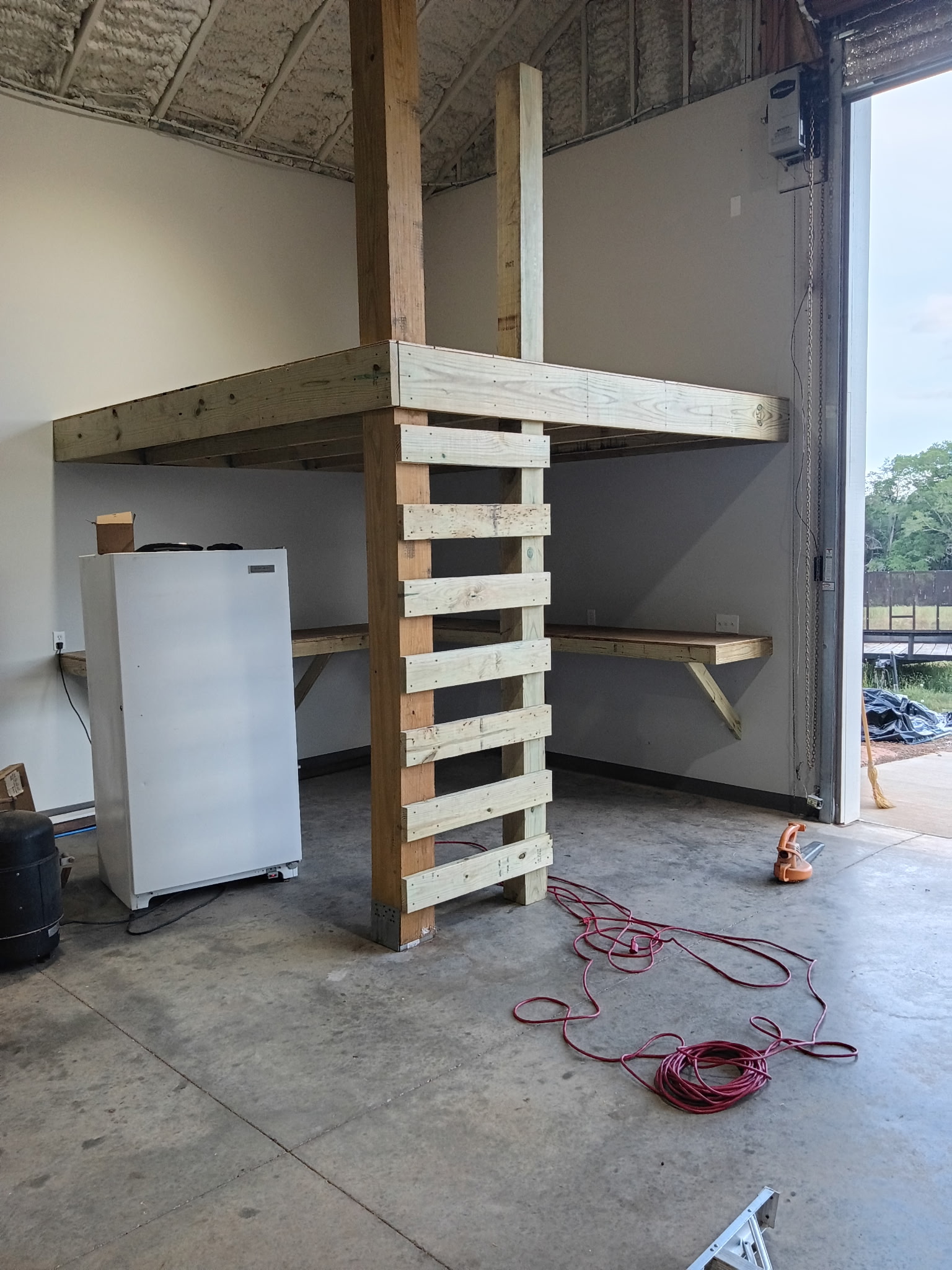 Custom-built garage loft and wall shelves with vertical wood ladder, made on-site.