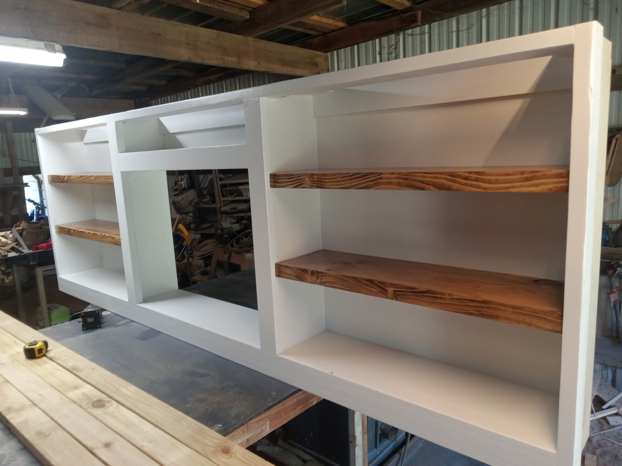 Custom white-finished media built-in with stained floating shelves, photographed in the workshop before install.