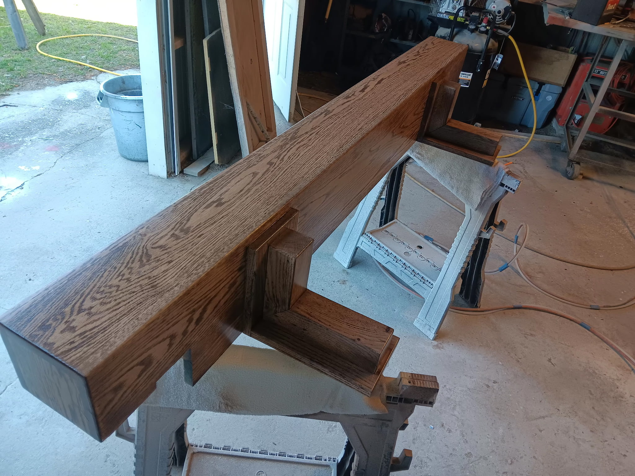 Stained solid oak mantle on sawhorses inside the workshop, hand-finished.